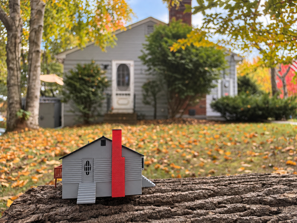 Printed house miniature on a log with the real house behind it